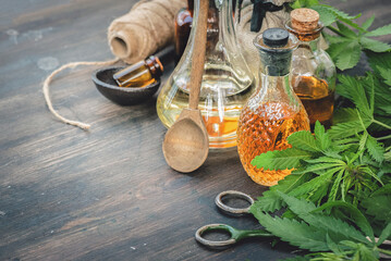 Cannabis CBD oil bottles and green plant leaves on dirty wooden table background.