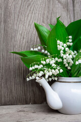 lilies of the valley in a white teapot on a wooden background