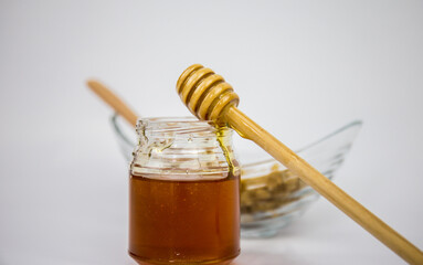 Glass jar with honey and a wooden stick on a white background