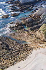 Gueirua beach, Asturias, Spain. Aerial view of rocky beach and a couple sitting in the white sand talking.