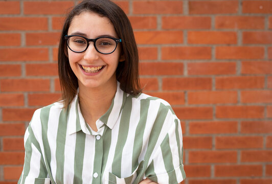 Business woman in glasses and striped shirt smiling at a brick wall. Copy Space for text.