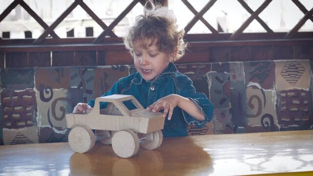 A boy plays with a cardboard homemade pickup truck on a yellow table in the gazebo. Children's entertainment in the fresh air.