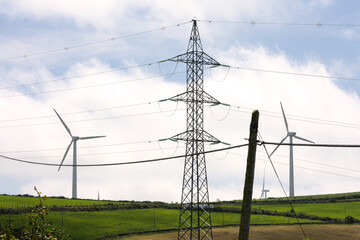 Horizontal view of three different types of energy, old electric post, modern electric post and wind turbine in summer green landscape.