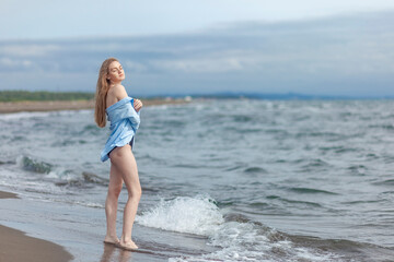 Fototapeta premium Beautiful young blonde girl in a blue shirt relaxing on the sea