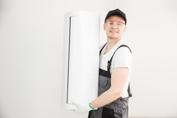 Male technician installs white air conditioner on wall