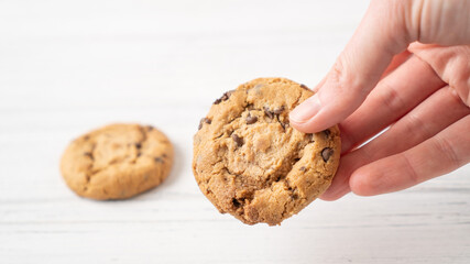 Chocolate chip cookie in hand. Hand holding cookie with chocolate drops on white wooden background. American cookie