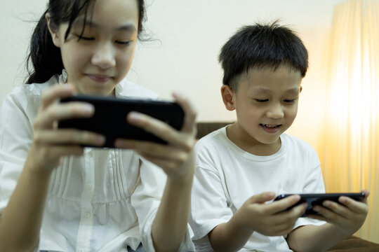 Two asian children people use smart phone and smile happily,sibling is relaxing enjoying,child girl playing online games on phone,kid boy watching movies,cartoon,having fun with mobile phone together