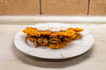 Ördöglángos on a white plate on a kitchen counter. Ördöglángos is a Hungarian rural food containing ground fired potato, meat, mushrooms and spices.