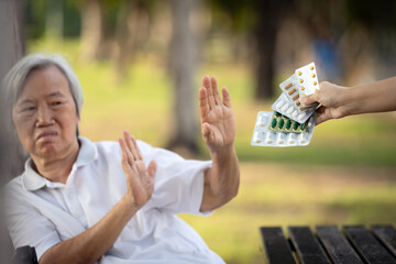 Hand of caregiver giving medicine pills and capsules to the elderly,asian senior woman refusing to...