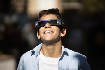 smiling boy watching an eclipse of the sun with eclipse glasses - obrazy, fototapety, plakaty