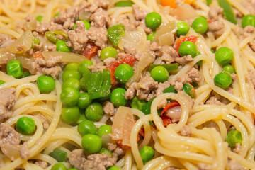 pasta, ground beef, peas, green peppers and chopped tomatoes over a pan.