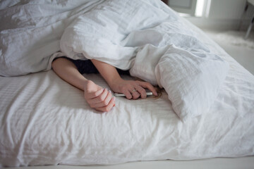 Obraz na płótnie Canvas Morning, the woman under the blanket, turns off the alarm clock