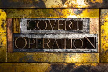 Photo of real authentic typeset letters forming Covert Operation text on vintage textured silver grunge copper and gold background