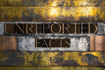 Photo of real authentic typeset letters forming Unreported Facts text on vintage textured silver grunge copper and gold background