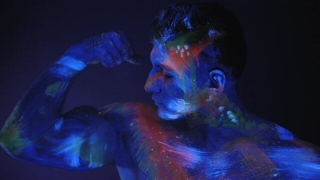 Portrait of a muscular guy with UV paint on his skin. Portrait of young man in UV paint. Bright fluorescent body art glows in darkness.