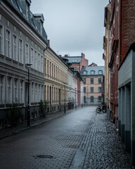 An empty cobblestoned street bordered with old colorful houses on a rainy day in Malmö, Sweden