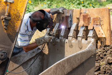 Man is welding the bucket of an excavator machine outside
