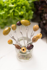 Composition of single green, black, stuffed, pitted and beautiful olives from Cerignola on forks ready for aperitif