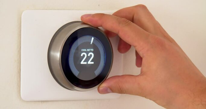 A persons hand cooling down the room temperature on centigrade celsius metrics using a smart thermostat during the summer on a white wall.
