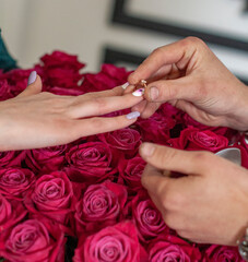 Betrothal ring on woman hand with pink bouqet of roses. Romantic event.