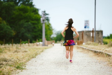 Woman running alone on dirt road, greenway on her back