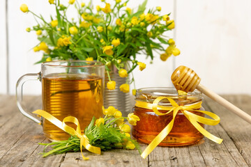 A jar of young honey and a Cup of hot tea with lemon on the background of a bouquet of yellow wild...