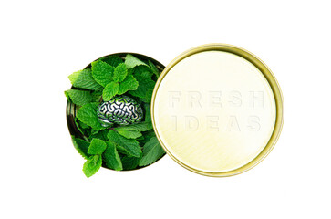Round tin box full of fresh green mint leaves and a steel copy of human brain on top. FRESH IDEAS text is embossed on the lid. Fresh thinking marketing concept.