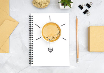 Light bulb symbol made of a fresh cup of coffee and a sketch on a spiral notebook. Office workplace flat lay. Refreshment and productivity concept. Boosting brain function with caffeine.