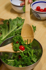 Close up of hands removing a salad in a metallic bowl with wooden spoons in a kitchen.