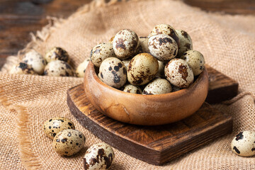 Fresh quail eggs in a wooden bowl on a brown wooden table. Raw quail eggs close-up on a culinary background. Concept of preparation for cooking