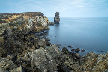 Long exposure seascape of the cliffs of Papoa island in Carvoeiro cape from the sea at sunrise in a cloudy day, Atlantic coast, Portugal