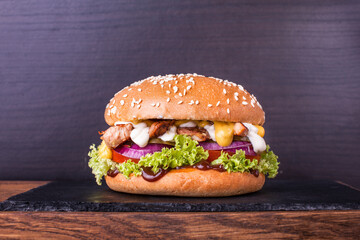 Craft beef burger with marinated chicken in sauce, cheese, fresh vegetables and barbecue sauce on a board with a stone and wooden deck over wooden background. For restaurant menu
