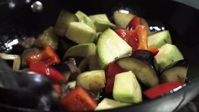 Vegetables are mixed with a tablespoon during cooking. Fried meat with vegetables in a pan