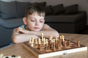 The serious child lost in thought playing chess. Playing board games, on coronavirus quarantine. The child playing chess.