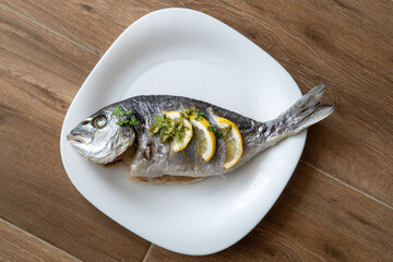 Dorada fish fried with lemon and parsley on a white plate