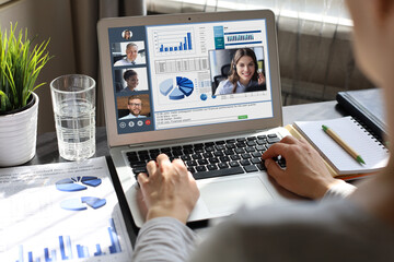 Business woman in headphones talking to her colleagues in video conference. Multiethnic business team working from home using laptop, discussing financial report of their company.