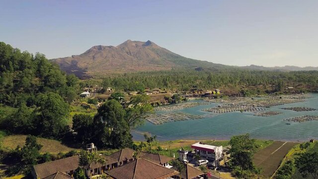 Aerial view of a tropical fishing village lake with a view of volcano craters. Panoramic drone flight over peaceful village in countryside Fish cages on water. Traditional fish breeding system.