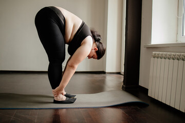 Obraz premium Fitness, home training, flexibility. Overweight woman doing stretching exercises on a fitness mat at her living room. Healthy lifestyle