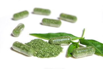 Dry green leaves andrographis paniculata or kariyat (fah talai jone) powder in capsule with white background, a Thai traditional herb and has antipyretic properties close-up.