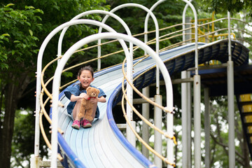 テディベアと一緒に滑り台で遊ぶ女の子