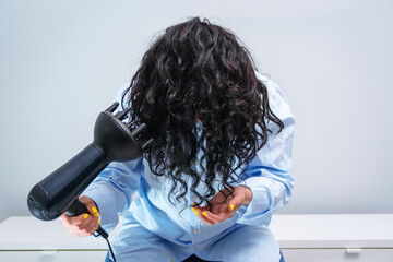 Woman makes herself curly hairstyle. Haircare concept. Girl drying hair at home.