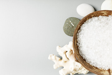  White sea bath salt in a coconut bowl, coral and stones on a gray background. Spa and relaxation concept. copy space