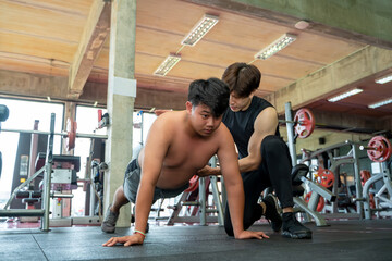 Personal trainer assisting overweight man doing push ups in a gym,Fitness,Weight loss concept.