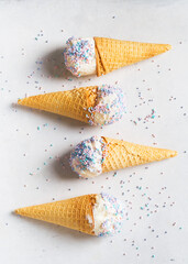 White vanilla ice cream scoop in waffle cone with sprinkles on light grey background