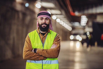 Cheerful smiling bearded arabian investor in vest, with headscarf on head standing in building in...