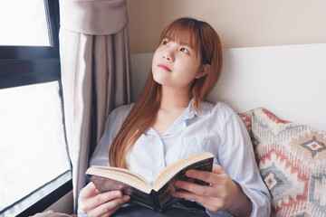 Closed up image of an asian woman reading a book comfortably. Isolating at home.