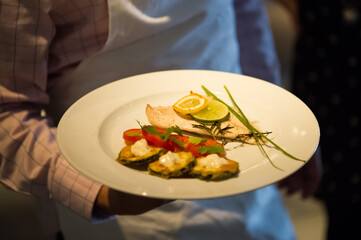 Fried zucchini rings served with fish on a white plate. Darkness in the room