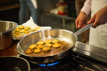 Man hands holding a frying pan, cooking zucchini rings.