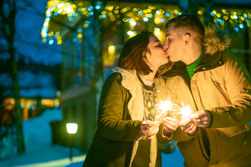 Kiss.  Lovers celebrate Christmas. Wife and husband celebrate new year. Guy kisses the girl. Lovers with sparklers. Celebrating the new year in the country. Organization of Christmas travel.