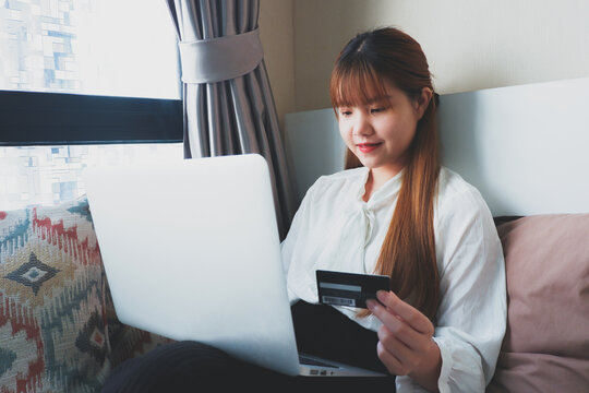Closed up image of a woman happily using a credit card to shop online in a laptop at home.